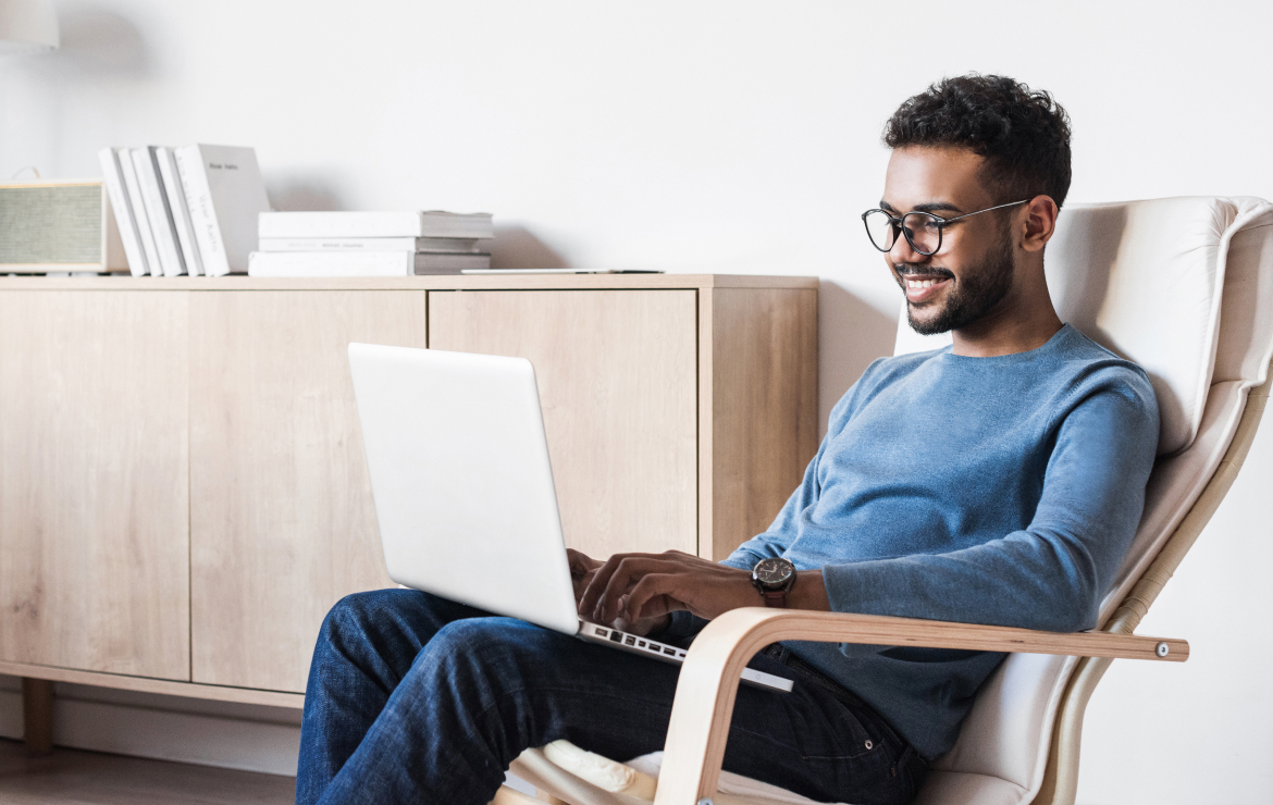 Man wearing glasses sitting in living room while scrolling on laptop